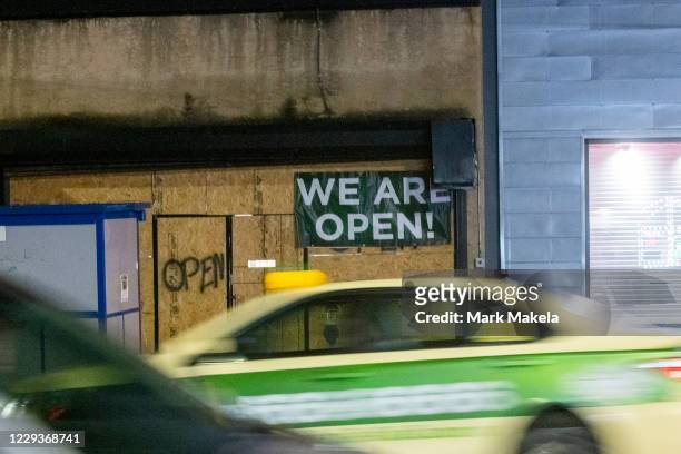 Cars blur past a boarded up store with a draped banner and spray painted "OPEN" notices after looting on October 30, 2020 in Philadelphia,...