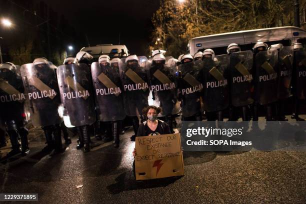 Protester wearing a face mask with a placard sits in front of the riot police forces guarding Kaczynski's house during the demonstration. Tens of...