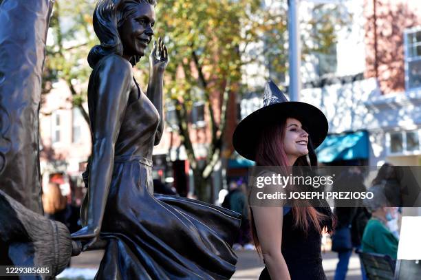 Woman dressed as a witch stands next to the Bewitched statue of Elizabeth Victoria Montgomery on Halloween in Salem, Massachusetts on October 31,...