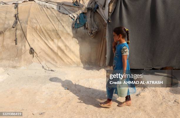Displaced Syrian child carries a jug on water in one of the alleys of an overcrowded displacement camp near the village of Qah near the Turkish...