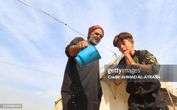 Young boy washes his face with water poured from a jug by an elderly man, in an overcrowded displacement camp near the village of Qah near the...