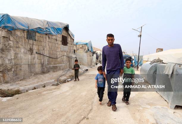 Hassan Sweidan walks with children in one of the alleys of an overcrowded displacement camp near the village of Qah near the Turkish border in...