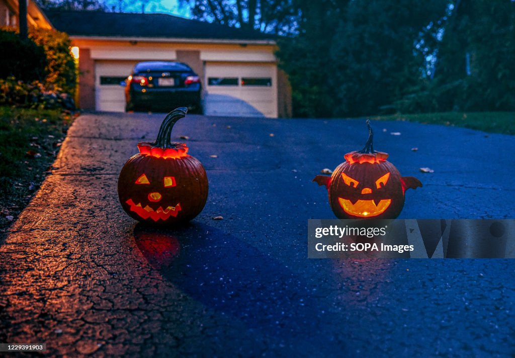 Two jack-o-lanterns glow on a driveway as the sun sets...