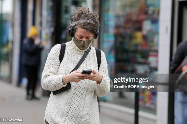 Woman wearing a face mask uses her phone while walking on the street.