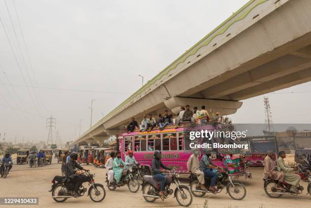 Passengers travel on the rooftop of a bus past an elevated corridor of the Green Line Bus Rapid Transit System in Karachi, Pakistan, on Saturday,...