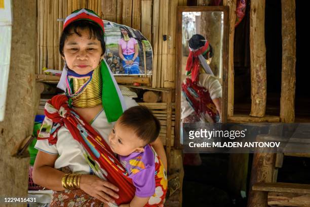 Long Neck Karen woman carries a baby in Baan Tong Luang hill tribes village situated some 30km west of Chiang Mai on November 2, 2020. - Created as a...