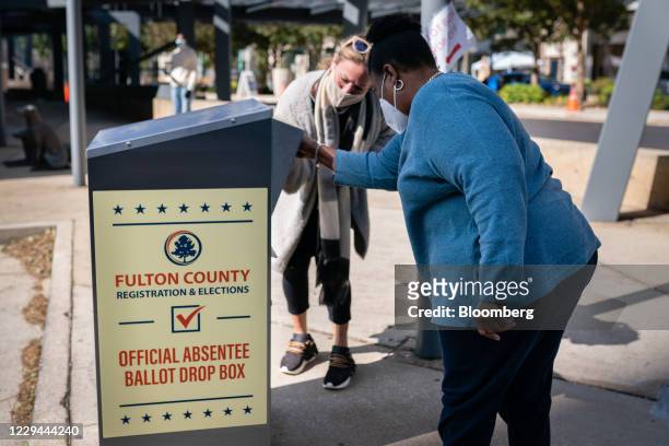 An election observer assists a voter as she drops off an absentee ballot into a drop box outside a polling location for the 2020 Presidential...