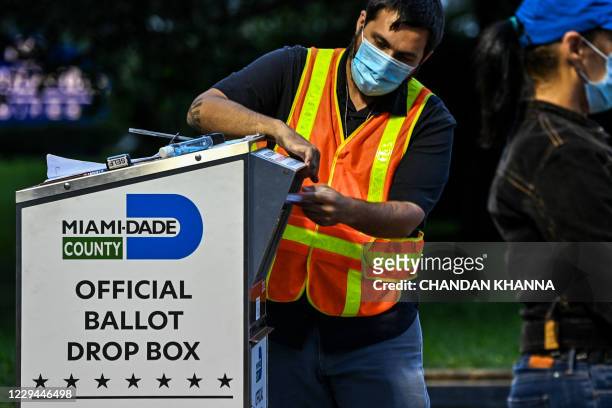 Poll worker helps a voter put as she drops off her mail-in ballot at an official Miami-Dade County drive-thru ballot drop box at the Miami-Dade...