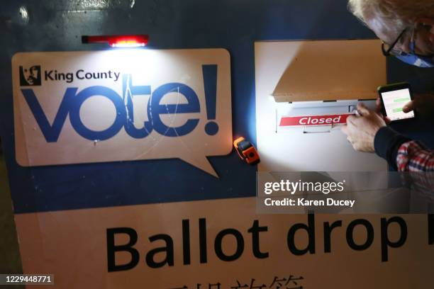 King County Elections worker Jules James locks the ballot drop box with a closed sign blocking the slot at the Seattle Public Library - Ballard...