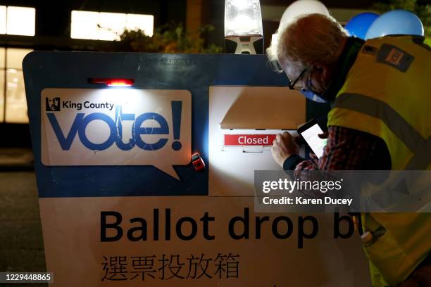 King County Elections worker Jules James locks the ballot drop box with a closed sign blocking the slot at the Seattle Public Library - Ballard...