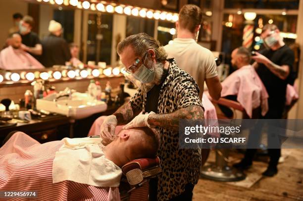 Worker wearing a face masks or coverings due to the COVID-19 pandemic, gives a customer a wet shave inside a barber's shop in central Manchester,...