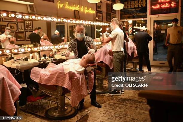 Worker wearing a face masks or coverings due to the COVID-19 pandemic, gives a customer a wet shave inside a barber's shop in central Manchester,...