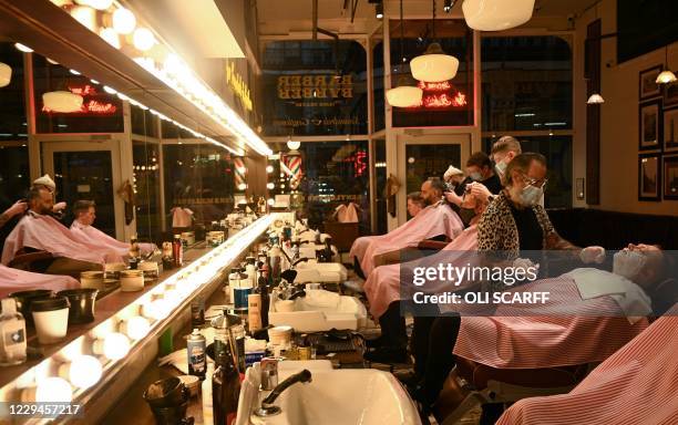 Worker wearing a face masks or coverings due to the COVID-19 pandemic, gives a customer a wet shave inside a barber's shop in central Manchester,...