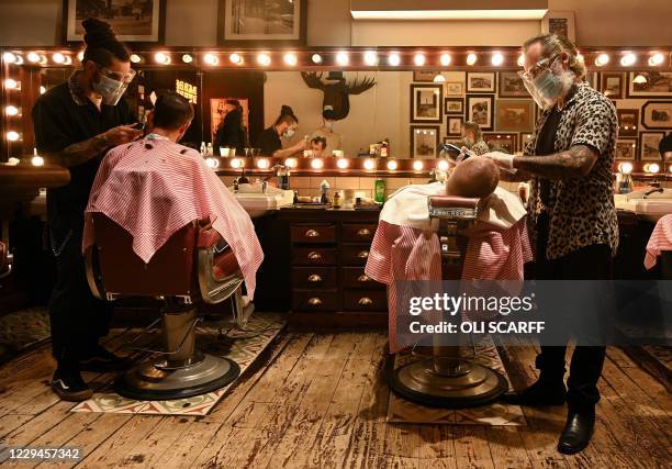 Worker wearing a face mask or covering due to the COVID-19 pandemic, gives a customer a wet shave inside a barber's shop in central Manchester, north...