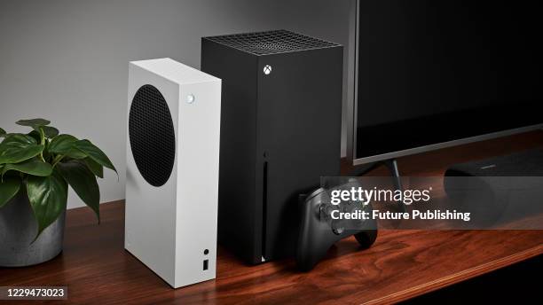 Living room with a pair of Microsoft home video game consoles, including an Xbox Series S and Xbox Series X, alongside a television and soundbar,...