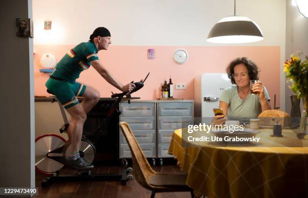 In this photo illustration a man rides a bicycle in his kitchen while the woman is having dinner. On November 04, 2020 in Bonn, Germany.