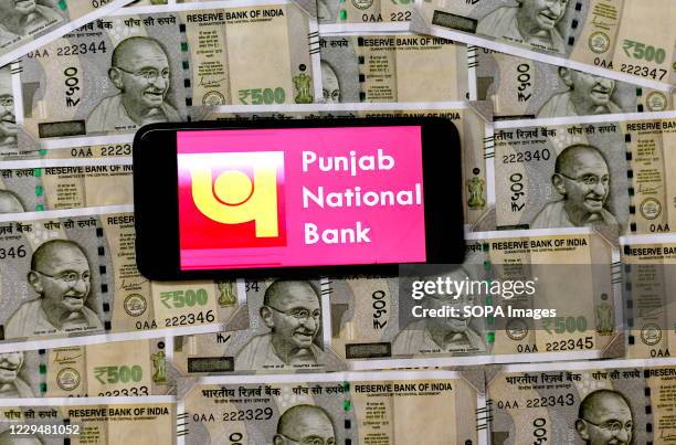 In this Photo illustration, Punjab National Bank Logo seen displayed on a smartphone with Indian Currency note illustrations on the background.