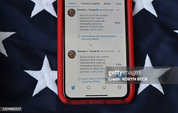 This illustration photo shows a mobile phone placed on a US flag with Tweets from US President Donald Trump masked with warnings imposed by Twitter...