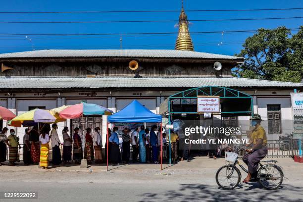 Man cycles past people queuing to vote in the elections at a polling station in Mandalay in November 8, 2020.