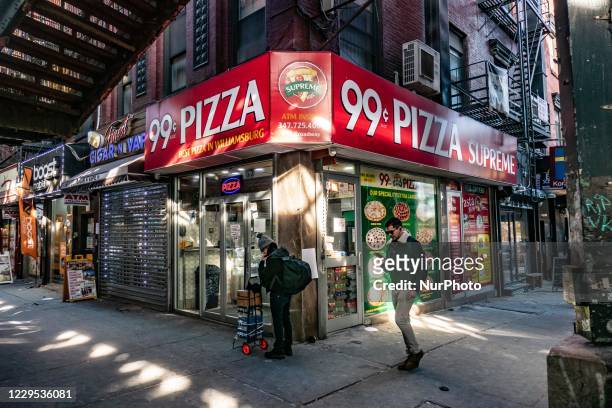 Man passing in front of 99c dolar slice pizza holding his phone and walking. Daily life view of the road and street under the subway railroad...