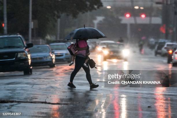 Man holds her daughter as he crosses the road during a heavy rain and wind as tropical storm Eta approaches south of Florida, in Miami, Florida on...