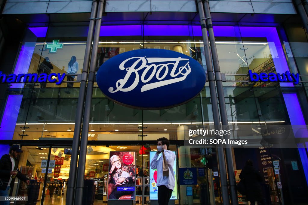 A man wearing a face mask walks past a branch of Boots on...