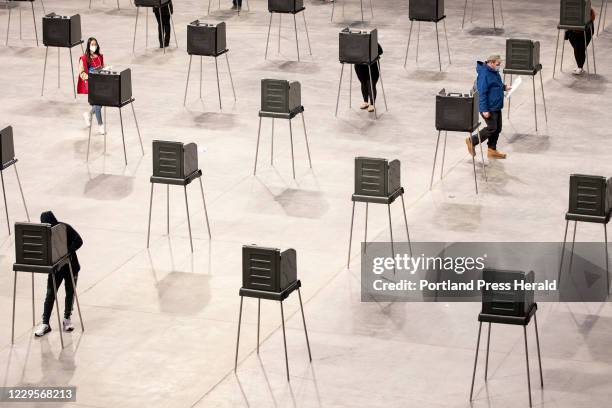Poll worker walks over to sanitize a voting booth after a voter leaves to walk their ballot over to the machines at Cross Insurance Center on...