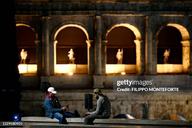 People wearing protective face masks play cards by the Colosseum in Rome on November 11 during the government's restriction measures to curb the...