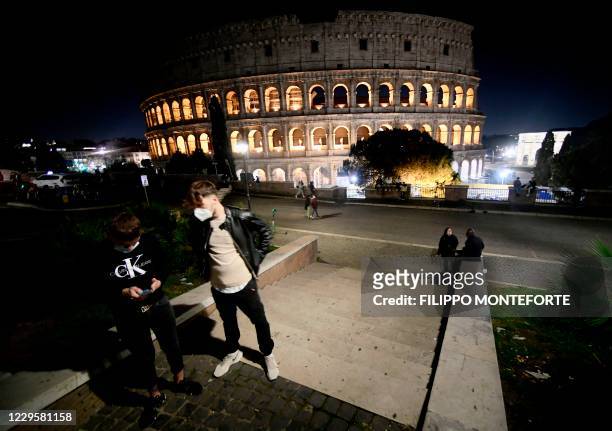 People wearing protective face masks look at their smartphones near the Colosseum in Rome on November 11 during the government's restriction measures...