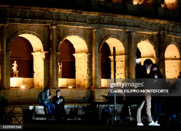 People wearing protective face masks look at their smartphones in front of the Colosseum in Rome on November 11 during the government's restriction...