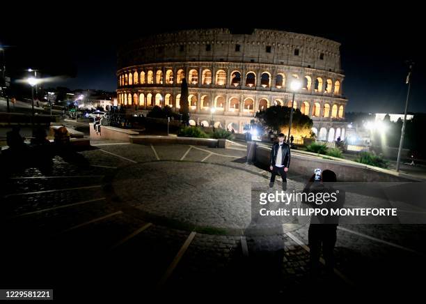 People wearing protective face masks take pictures in front of the Colosseum in Rome on November 11 during the government's restriction measures to...