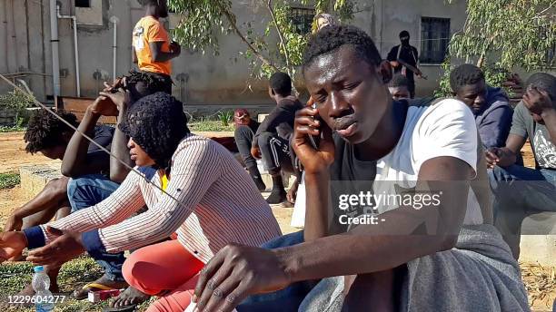 Migrant, who survived a deadly shipwreck, speaks on the phone as he gathers with other survivors in an area on the coast of al-Khums, a port city 120...