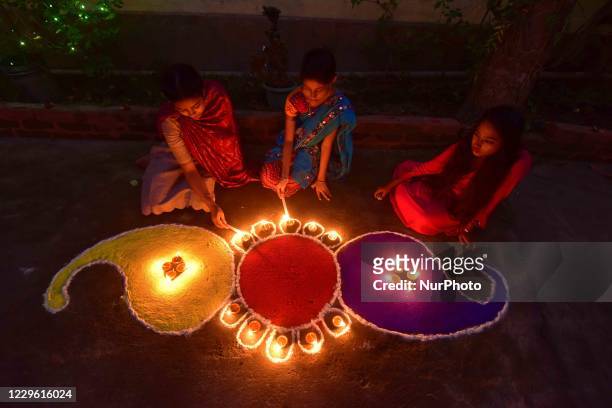 Girls pose after lighting oil lamps around a "Rangoli", a traditional pattern made from coloured powders and flower petals outside their home to...