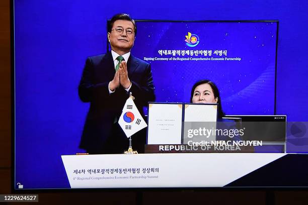 South Korea's President Moon Jae-in claps as South Korea's Minister for Trade Yoo Myung-hee holds up the signed agreement, as seen on a TV monitor,...