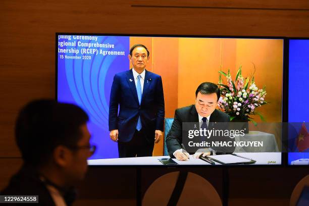 Japan's Prime Minister Yoshihide Suga stands next to Japan's Minister of Economics, Trade and Industry Hiroshi Kajiyama as he signs the agreement, as...