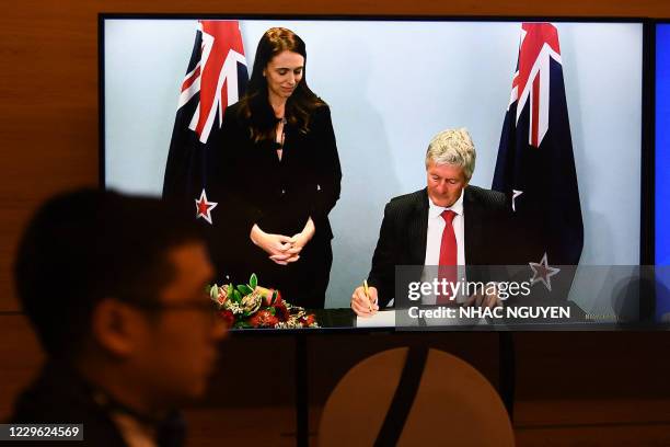 New Zealand's Prime Minister Jacinda Ardern looks on as New Zealand's Trade Minister Damien O'Connor signs the agreement, as seen on a TV monitor,...