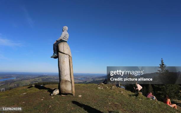 Dpatop - 14 November 2020, Bavaria, Rettenberg: A boy sits on the two-meter-high wooden penis sculpture on the ridge of the Grünten. This unusual...