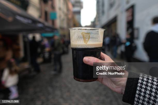 Person holds a pint of Guinness in a plastic cup seen outside The Ha'Penny Bridge Pub in the center of Dublin. On Saturday, November 14 in Dublin,...
