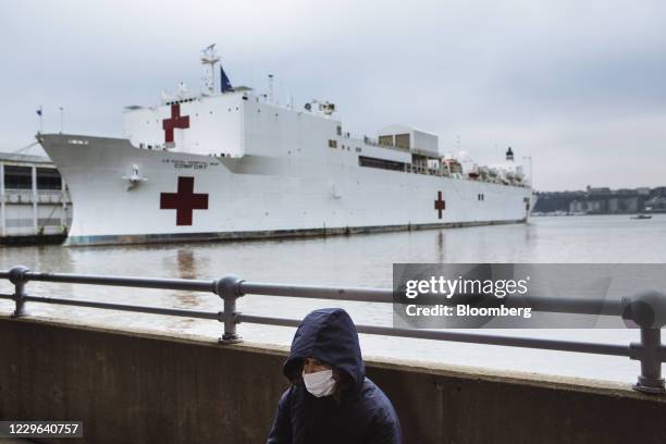 Bloomberg Best of the Year 2020: A person wearing a protective mask sits in front of the USNS Comfort hospital ship which will handle hospital...