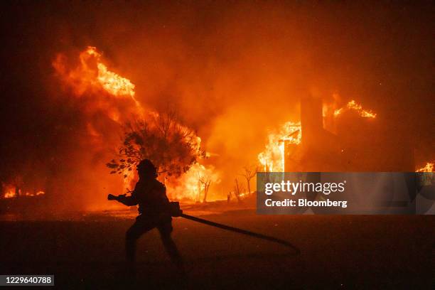 Bloomberg Best of the Year 2020: A firefighter carries a hose as buildings burn in the Skyhawk Park neighborhood of East Santa Rosa during wildfires...