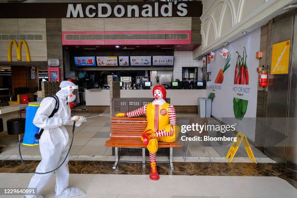 Bloomberg Best of the Year 2020: A worker wearing Personal Protective Equipment sanitizes a bench and novelty Ronald McDonald figure outside a...