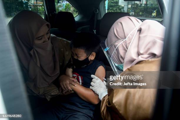 Boy receives a diphtheria vaccine from a health worker at a drive-thru vaccination site amid the COVID-19 outbreak at Pondok Betung village in South...