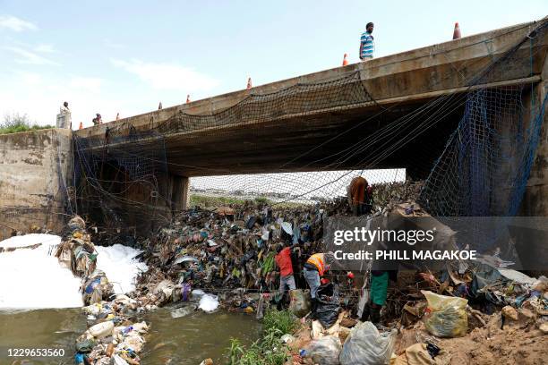 Man walks over a bridge while workers from Fresh.ngo remove plastic deluge from litter trap nets and long line cables that was washed down the...