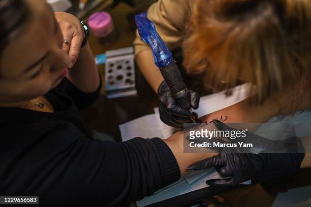 Hamide Faqiri, left, watches as Soraya Shahidy, right, a tattoo artist, inks the tattoo ONever Give Up,O on her forearm, at the Angel Beauty Salon in...