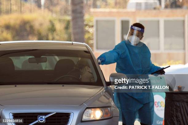 Testing site staff member conducts a temperature check at a drive-up testing site at the Orange County Fairgrounds in Costa Mesa, California,...