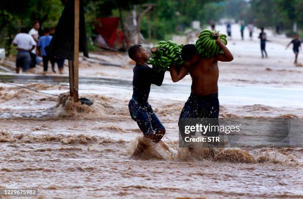 Yougsters carry bananas as they wade along a flooded street in El Progreso, department of Yoro, Honduras on November 18 after the passage of...