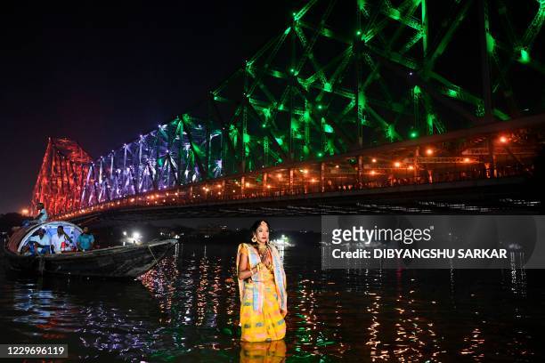 Hindu devotee takes part in a ritual to worship the sun on the banks of the Ganges River as the iconic Howrah Bridge is seen illuminated during the...