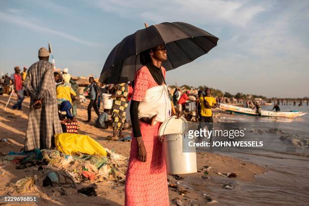 Woman carrying a baby in a sling onher back waits to buy fresh fish at the fishing port in Mbour on November 16, 2020. - Mbour has in the recent...