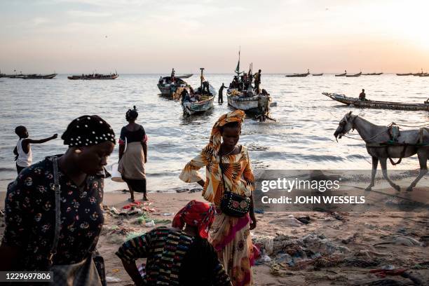 Women wait to buy fish off incoming boats at the fishing port in Mbour on November 16, 2020. - Mbour has in the recent months been a popular...