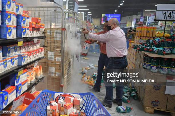 An employee uses a fire extinguisher after demonstrators set products on fire and threw others to the floor at a supermarket Carrefour in Sao Paulo,...